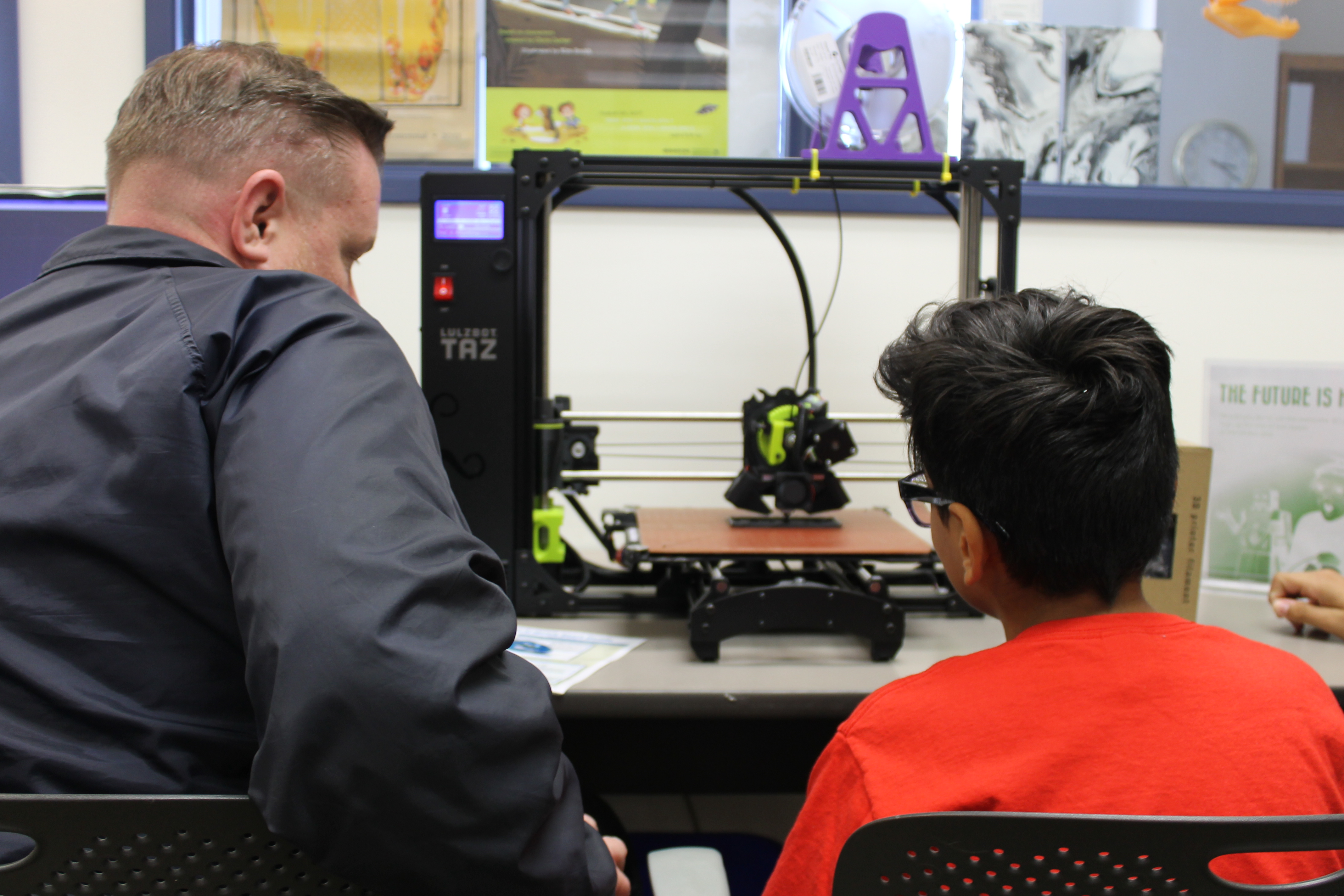 Photo of a man and a boy looking at and using a 3D printer