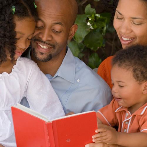 close crop of two smiling children reading with two smiling adults