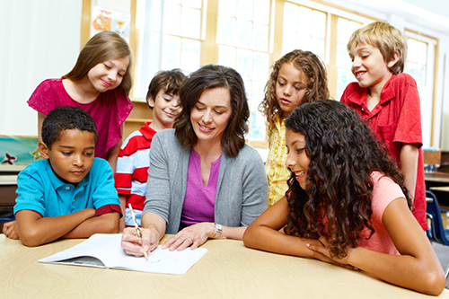 group of children sitting and standing around adult who is writing in homework book