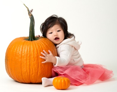 Baby girl in pink skirt hugging a pumpkin