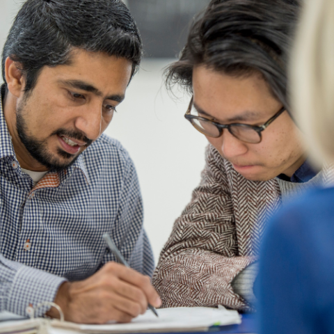 man with beard writing on paper with woman with glasses looking at paper