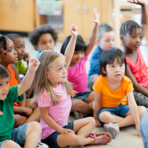 group of preschool age children with hands raised like answering a question