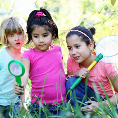 three school age children in grass with magnifying glass