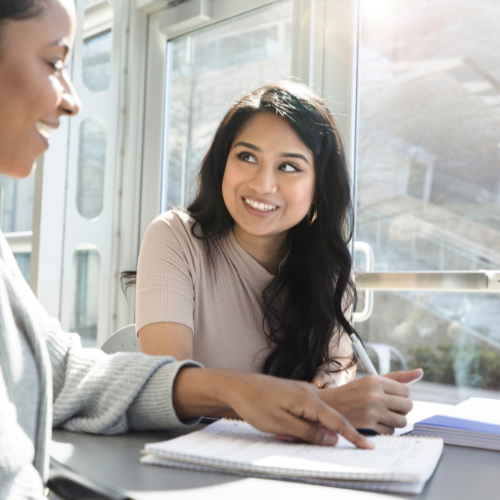 woman with pencil and paper smiles up at person pointing to paper