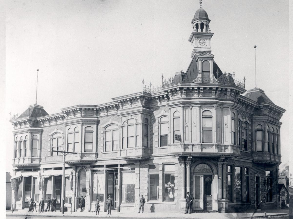 Historical black and white photo of the two story Bank of Oceanside with a clock tower that housed the first Library, circa 1904 