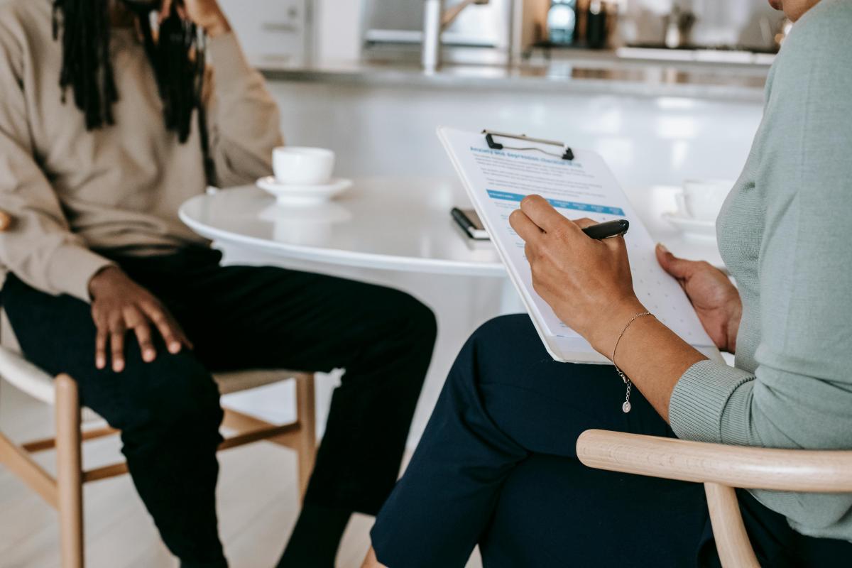 image of two individuals sitting across from each other, one is interviewing the other. 